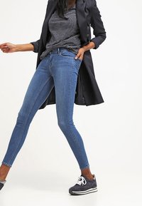 Jeans de mezclilla azules ajustados combinados con una camiseta de rayas negras y un blazer negro, llevados con zapatillas oscuras, con un diseño ceñido.