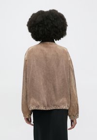 Καφέ μπουφάν από κορντόρι με άνετη γραμμή, ριγωτή υφή, ελαστικά μανίκια και ολόκληρη πλάτη, φορεμένο πάνω από μαύρο ένδυμα.