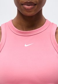 Κοντινό πλάνο ενός ατόμου που φοράει ροζ αθλητικό τοπ Nike χωρίς μανίκια με λευκό λογότυπο Nike στο στήθος.