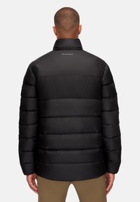 Svart pufferjacka med hög krage, quiltad design och matt finish. Har varumärkeslogotypen "MAMMUT" broderad på baksidan.