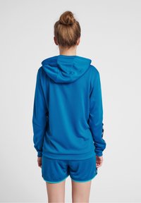 Niebieska sportowa bluza z teksturowanej tkaniny, z regulowanym kapturem i długimi rękawami, zestawiona z dopasowanymi niebieskimi szortami z elastycznym pasem.