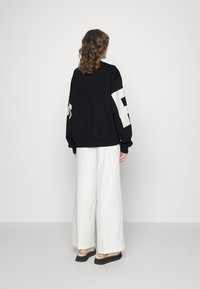 Sudadera negra de gran tamaño con un gran número blanco en la manga, combinada con pantalones anchos blancos y sandalias negras de plataforma. Tejido texturizado.