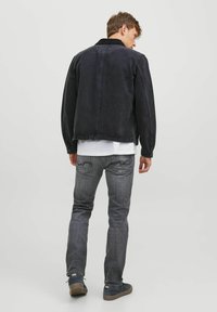 Jachetă din denim negru, croială relaxată, cu guler ribbelat și textură ușor estompată. Asortată cu blugi gri și adidași negri.