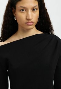 Czarna bluzka z odkrytymi ramionami i długimi rękawami. Gładki, elastyczny materiał; minimalne detale; lekko asymetryczny dekolt.