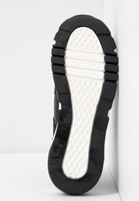 Semelle d'une basket avec semelle en caoutchouc noire et blanche, motif de grip texturé, et marquage de taille 37.