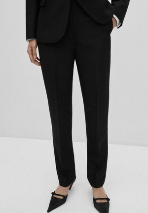 Pantaloni negri, croiți pe măsură, cu o tăietură dreaptă, având o textură netedă, față plată și buzunare laterale, asortați cu pantofi cu vârful ascuțit negri.