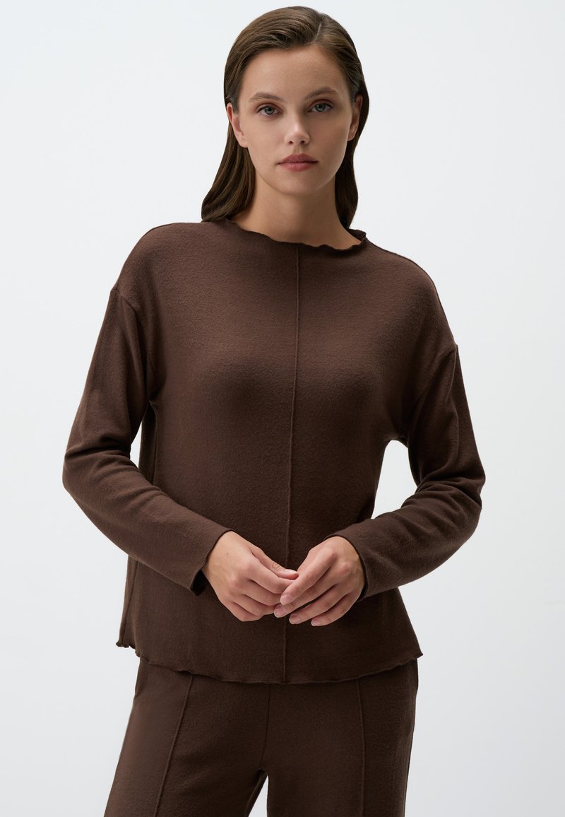 Camicia marrone a maniche lunghe con un colletto leggermente scallopato, tessuto morbido e dettagli cuciti. Visibile abbinata a pantaloni coordinati.