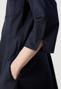 Navyblauwe jurk met een ontspannen pasvorm. Heeft korte mouwen met uitsneden, een opgestikte zak en een zachte textuur, die een minimalistisch ontwerp benadrukt.