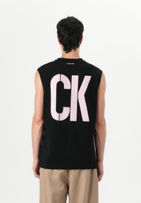 Svart ermeløs t-skjorte med stort rosa "CK" trykk på ryggen. Har rund hals og en avslappet passform. Laget av mykt stoff.