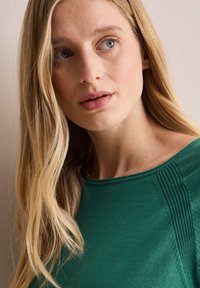 Top in maglia verde con scollatura rotonda e delicate finiture a coste sulle spalle, completato da una superficie di tessuto liscia.