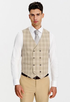 Mężczyzna ubrany w beżową, dwurzędową kamizelkę w kratę, białą koszulę wizytową, szary krawat, beżowe spodnie i czarny pasek, stojący na białym tle.