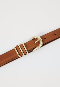 Bruine leren riem met een gouden metalen gesp met drie horizontale accenten. Soepele textuur met meerdere verstelgaten langs de band.