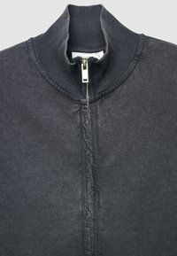 Dunkelgraue, gerippte Jacke mit hohem Kragen und silbernem Frontreißverschluss, teilweise hochgezogen, wobei der Kragen und der obere Stoffbereich sichtbar sind.