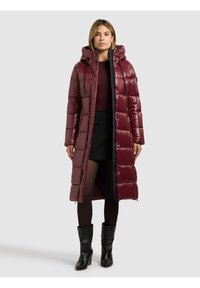 Bordový prošívaný kabát s lesklým povrchem, kapucí a předním zipem. Má vodorovný prošívaný vzor a černé detaily, sahá do poloviny lýtek. Černé boty.