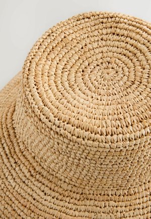 Woven straw hat with a flat circular top and wide brim, featuring a natural beige color and a textured, intricate pattern.
