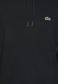 Sweat à capuche noir en tissu doux, avec une poche kangourou, un cordon de serrage réglable et un petit logo crocodile vert sur la poitrine.