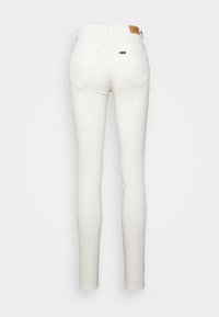 Jeans blancos ajustados de tiro alto, con dos bolsillos traseros y una etiqueta texturizada en la cinturilla. Fabricados con una tela elástica, de textura suave.