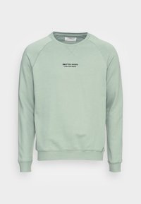 Sudadera verde claro con puños y dobladillo acanalados. Presenta un cuello redondo y texto impreso "ARTICULOS ARTESANALES - PIER ONE DENIM" en el pecho.