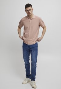 Lys rosa polo skjorte laget av bomull, med krage og korte ermer, kombinert med blå jeans og hvite sneakers.
