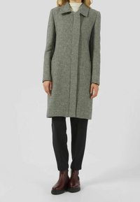 Abrigo de patrón de pata de gallo en gris y negro, con corte recto, cuello y cierre frontal oculto. Llevado con pantalones negros y botas burdeos.