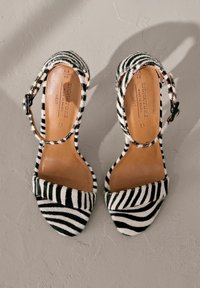 Sandales à talons hauts noir et blanc rayées avec une finition texturée semblable à de la fourrure, dotées d'un bout fermé et d'une bride à la cheville réglable.