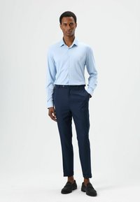 Lichtblauw overhemd met kraag, dichtgeknoopt, gecombineerd met donkerblauwe op maat gemaakte broek. Zwarte loafers. Glad textuur, nauwsluitende stijl, minimalistisch ontwerp.