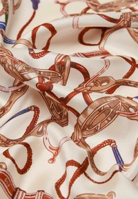 Siidkangas, millel on kreemivärvi taust ja keerulised pruunid, punased ja sinised ratsateemalised mustrid, mis kujutavad pehmeid ohje ja köisi.