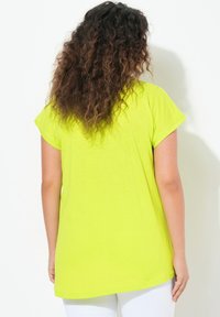 Camiseta verde lima de manga corta y dobladillo ligeramente curvado, fabricada con un tejido suave y ligero, vista desde la parte posterior.