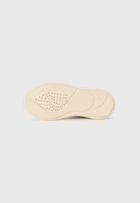 Suela de zapatilla en goma color blanco roto, con patrones texturizados, surcos para agarre y orificios de ventilación para transpirabilidad.