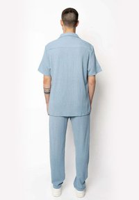 Ensemble en deux pièces bleu clair composé d'une chemise à manches courtes et d'un pantalon assorti, fabriqu�é à partir d'un tissu texturé avec une coupe décontractée.