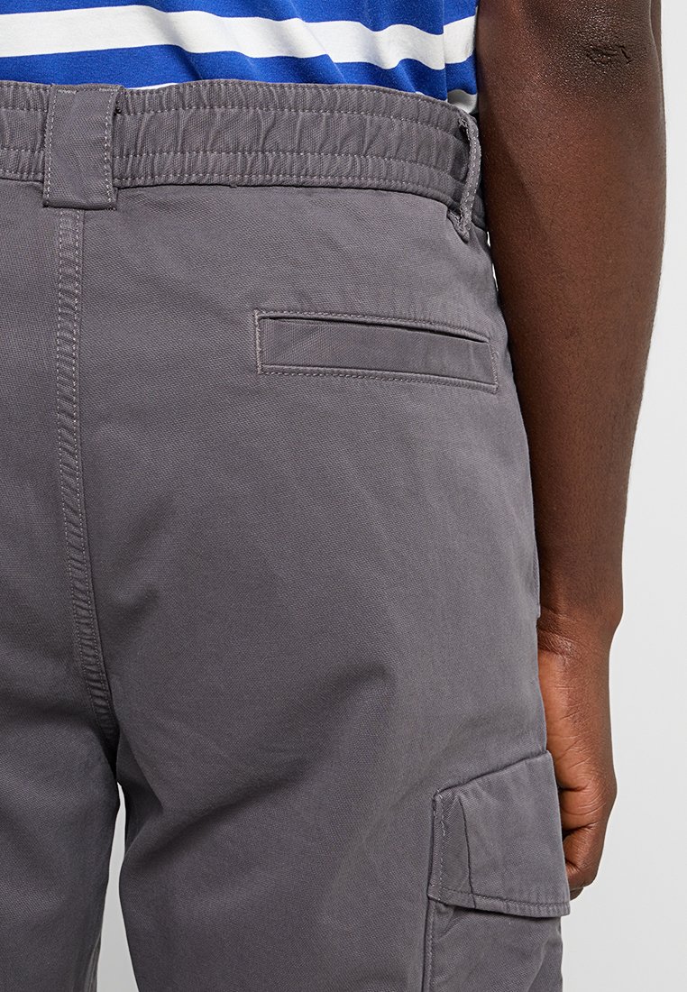 Pantalons cargo gris avec une taille élastique, dotés d'une poche arrière et de poches latérales en tissu durable. Texture lisse, design décontracté.
