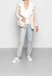 Blazer beige a righe con colletto bianco arricciato sopra un maglione bianco, abbinato a jeans in denim azzurro chiaro e sneakers bianche con platFORMA.
