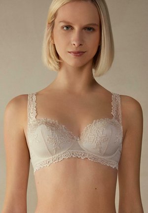 Beige bh met kantafwerking, van een lichtgewicht stof, met onderdraadondersteuning en decoratieve details langs de cups en bandjes.