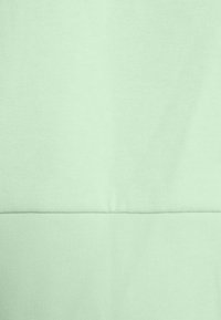 Tissu vert clair avec une couture horizontale divisant les parties supérieure et inférieure, montrant la texture tricotée et les détails de couture.