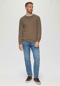 Brūns džemperis ar ribotām aprocēm, zilas džinses un brūnas sporta kurpes. Apģērbs ir ar ikdienišķu dizainu, ar apaļu kakla izgriezumu un šauru piegriezumu.