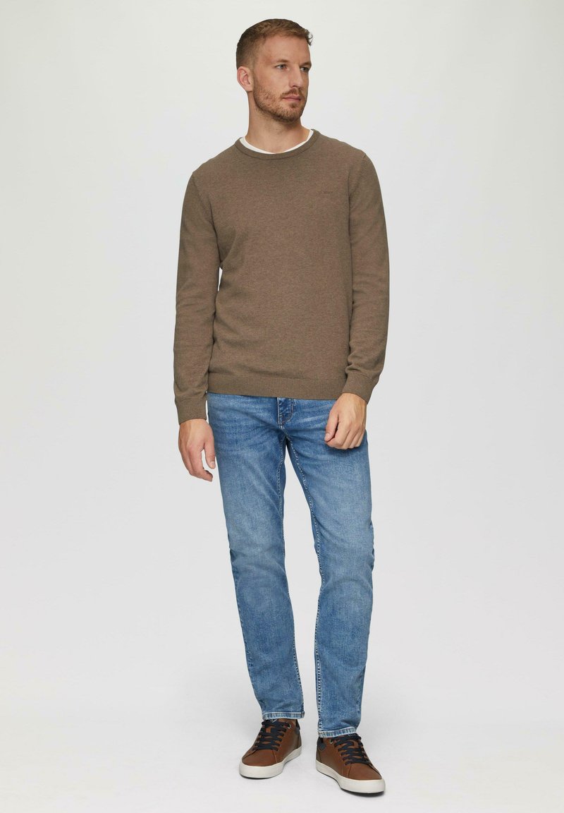 Brūns džemperis ar ribotām aprocēm, zilas džinses un brūnas sporta kurpes. Apģērbs ir ar ikdienišķu dizainu, ar apaļu kakla izgriezumu un šauru piegriezumu.