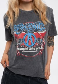 Gray, short-sleeve graphic t-shirt featuring blue and red Aerosmith logo with a peace symbol, dice, and "Deuces Are Wild" text.