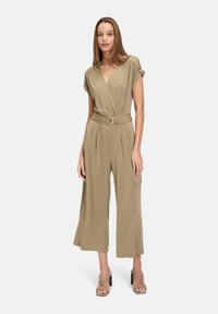 Olivgrön jumpsuit med omslagdesign, korta ärmar, bälte i midjan, vida ben och sidofickor. Mjuk, slät tyg och minimalistisk stil.