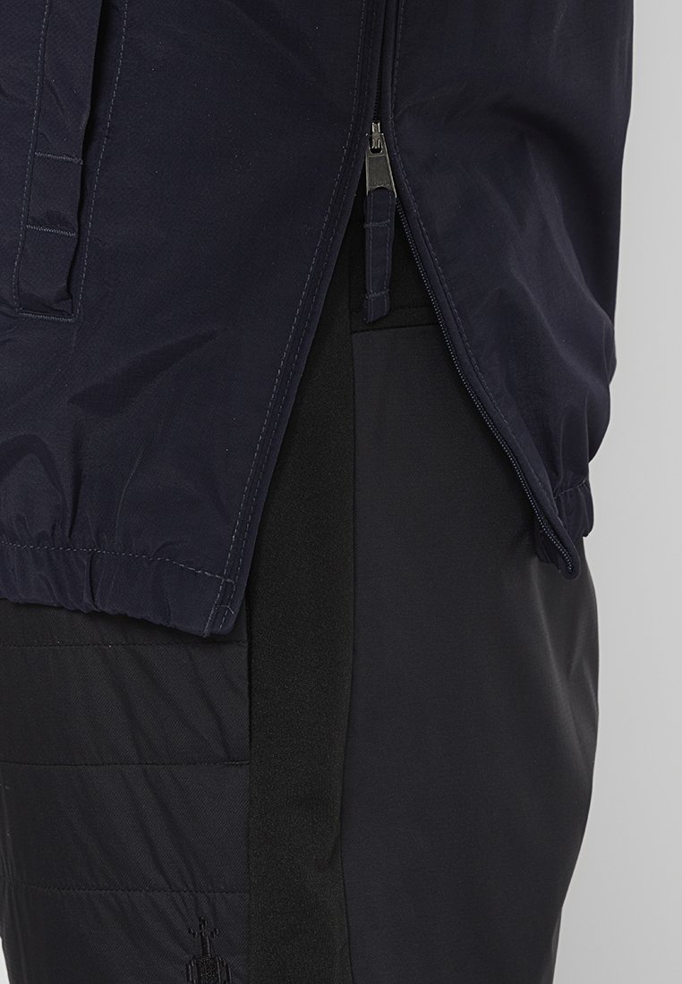 Rompevientos navy con un acabado texturizado, puños elásticos y cierre de cremallera. Combinado con pantalones negros que presentan detalles acolchados.