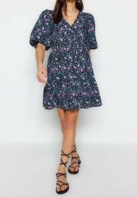 Sukienka w kwiaty w granatowym kolorze z bufkami na krótkich rękawach, głębokim dekoltem w kształcie V oraz warstwową, rozszerzaną spódnicą. W połączeniu z czarnymi sandałami na paski.