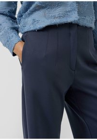 Lichtblauw gestructureerd topje met franjes, gecombineerd met marineblauwe, op maat gemaakte broek met gladde stof, zijzakken en kreuklijnen.