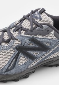 Grå och marinblå träningsskor tillverkade av mesh och syntetiska material, med en texturerad yta, framträdande logotyp och en robust yttersula.