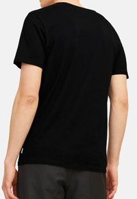 Sort bomulds t-shirt med rund hals og korte ærmer, med en lige kant og diskret branding på siden.