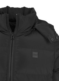 Doudoune noire avec col montant, fermeture éclair intégrale et boutons-pression. Présente une surface texturée avec un design matelassé et un patch logo.