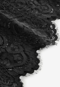 Fekete csipke anyag virágmintákkal, fodros, rojtos széllel, fehér háttéren.