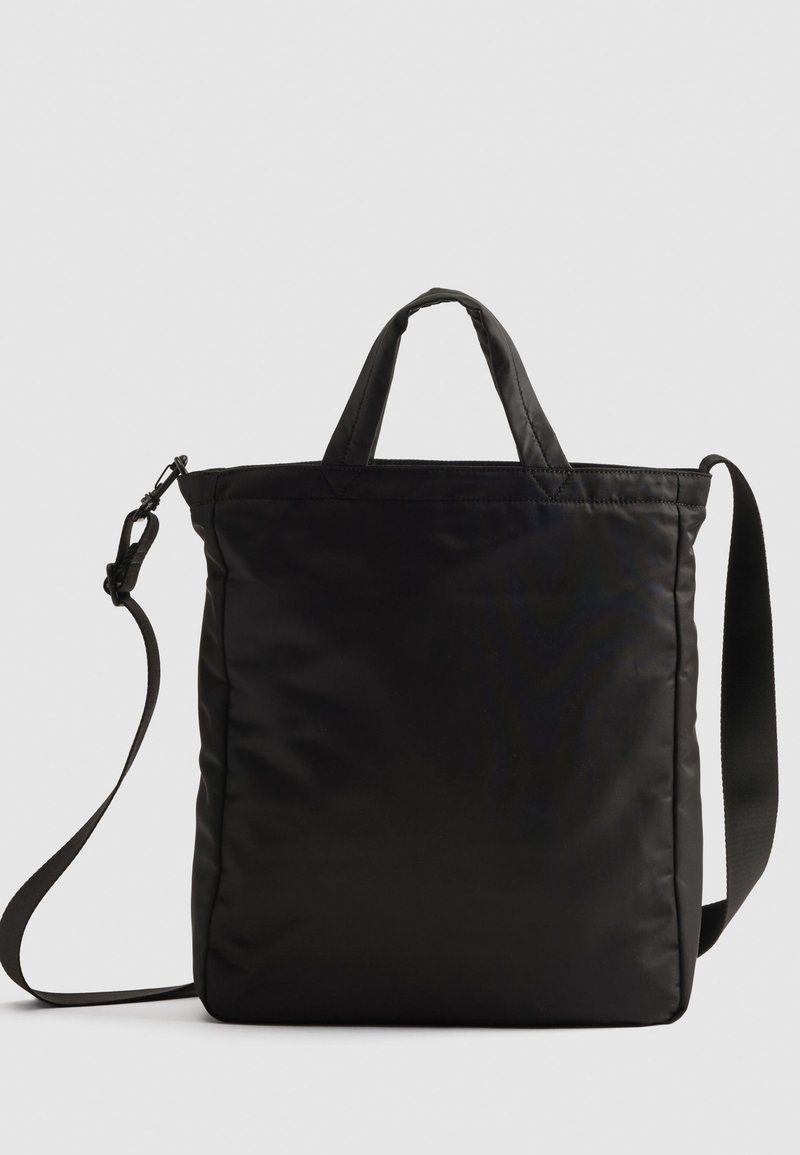 Bolsa de mano de nailon negro con asas cortas y una correa de hombro desmontable, que presenta un diseño acolchado elegante y acentos de hardware mínimos.