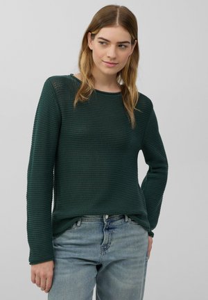 Groen gestructureerd sweater met lange mouwen en een ronde hals, gecombineerd met lichtblauwe spijkerbroek. Het materiaal lijkt geweven met een chunky patroon.