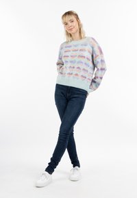 Helles blauer Strickpullover mit einem mehrfarbigen Wolkenmuster, kombiniert mit dunkelblauen Skinny-Jeans und weißen Sneakern.