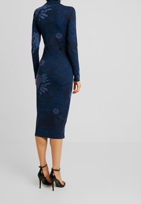 Navy floral bodycon dress with long sleeves and mock neck, featuring a textured pattern and a midi length, paired with black stiletto heels.