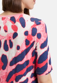 Short-sleeve top in lightweight fabric featuring a pink, red, and dark blue abstract pattern with a round neckline and visible seams.